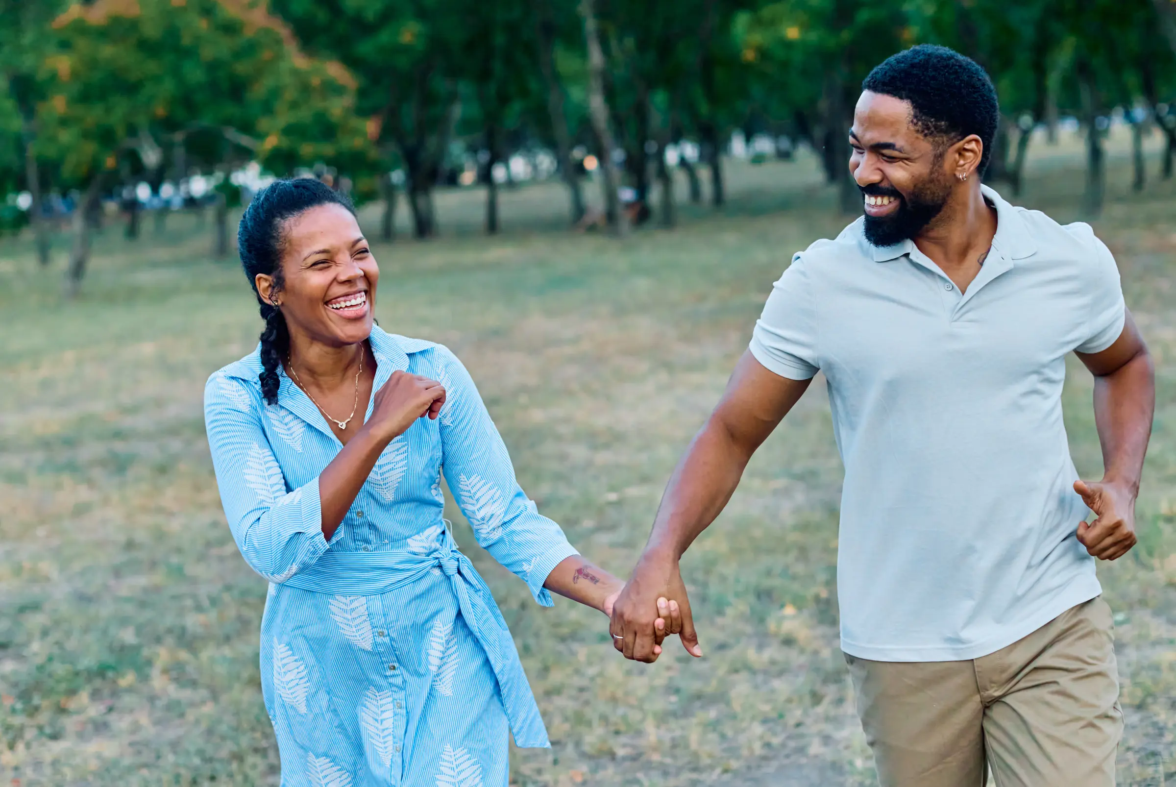 Couple laughing and holding hands on a walk in the park.
